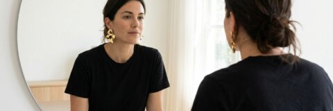 Persönlichkeit durch Mode ausdrücken: Frau mit auffälligen Ohrringen und schlichtem Outfit vor einem Spiegel